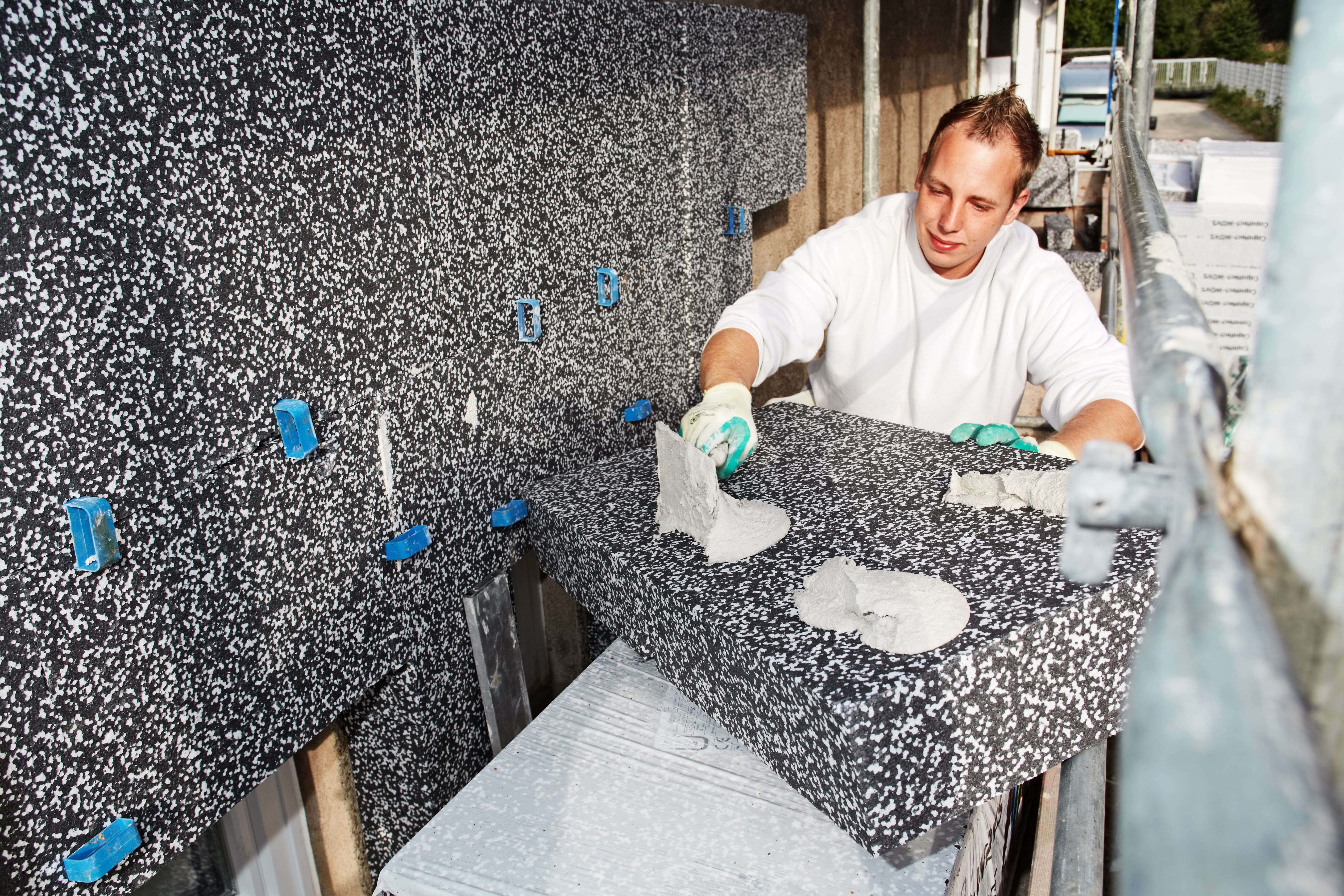 Handwerker dämmt die Fassade eines Hauses von außen auf einem Gerüst stehend
