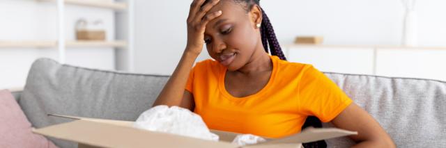 Eine junge Frau sitzt auf dem Sofa mit einem geöffneten Paket auf dem Schoß.