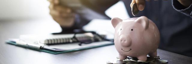 Sparschwein steht auf Münzen vor Notizblock und Taschenrechner