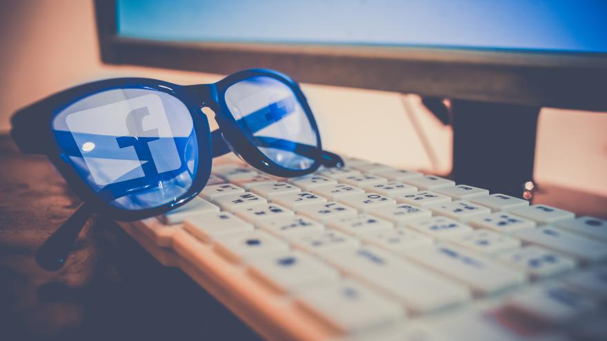 Auf einer Computertastatur liegt eine Brille, in der sich das Facebook-Logo spiegelt.