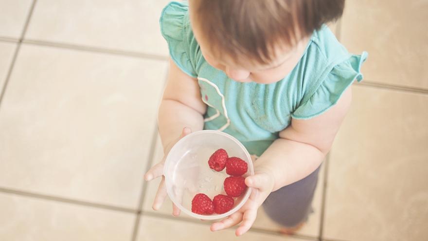 Ein Kleinkind trägt eine Schale mit Joghurt und Himbeeren