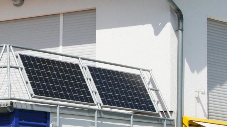 Außen an dem Geländer eines Balkons sind zwei Solarmodule montiert.