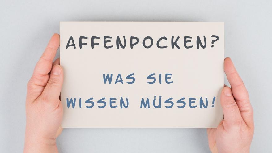 Ein Schild wird festgehalten. Es hat die Aufschrift "Affenpocken? Was Sie wissen müssen!".