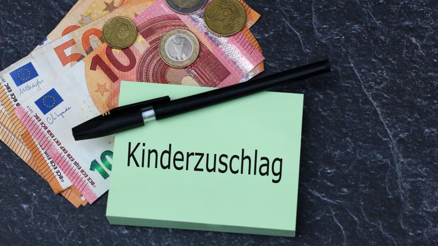 Zettel, auf dem das Wort Kinderzuschlag steht, ein Kugelschreiber sowie Geldscheine und Münzen