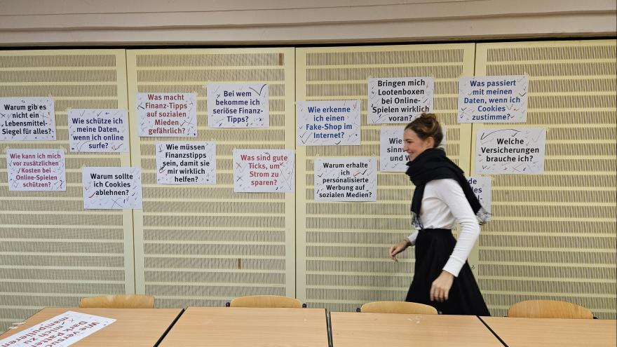 Eine june Frau geht an einer Pinwand vorbei, an der viele Zettel angepinnt sind