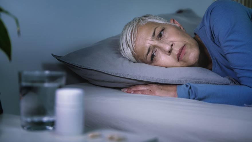 Eine schlaflose Frau liegt wach im Bett und schaut auf eine Dose mit Schlaftabletten