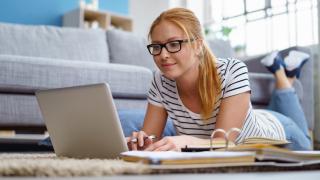 Junge Frau liegt am Boden und surft im Laptop nach Auktionsportalen für Zahnersatz