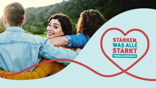 Eine lächelnde Frau blickt über ihre Schulter, während sie in einer Gruppe von drei Personen steht, die sich gegenseitig umarmen. Im Hintergrund ist eine grüne Landschaft zu sehen. Rechts im Bild befindet sich eine Grafik mit einem roten Herz aus einem Seil und dem Schriftzug: "STÄRKEN, WAS ALLE STÄRKT – VERBRAUCHERSCHUTZ" auf hellblauem Hintergrund.